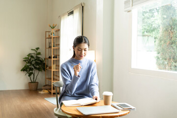 Young Asian woman enjoying a peaceful moment reading a book near window. Calm lifestyle, self-learning, and mindfulness at home.