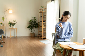 Young Asian woman enjoying a peaceful moment reading a book near window. Calm lifestyle, self-learning, and mindfulness at home.