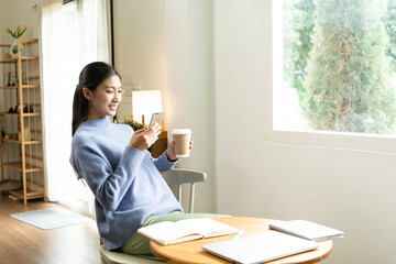 Young Asian woman enjoying a peaceful moment reading a book near window. Calm lifestyle, self-learning, and mindfulness at home.