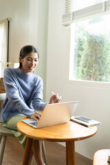 Young Asian woman enjoying a peaceful moment reading a book near window. Calm lifestyle, self-learning, and mindfulness at home.