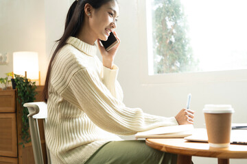 Young Asian woman enjoying a peaceful moment reading a book near window. Calm lifestyle, self-learning, and mindfulness at home.