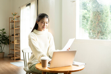 Young Asian woman enjoying a peaceful moment reading a book near window. Calm lifestyle, self-learning, and mindfulness at home.