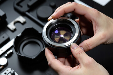 Technician's hands performing a precision repair and assembly of a professional camera lens with specialized tools in a workshop