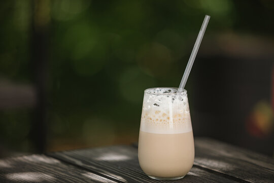 Close-up of an Iced coffee latte with frothy foam on a wooden garden table