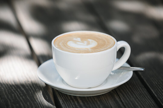 Close-up of a latte coffee on a wooden garden table in the sunlight