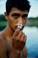 Introspective Young Man Holding Delicate Flower by Serene Lake at Dusk