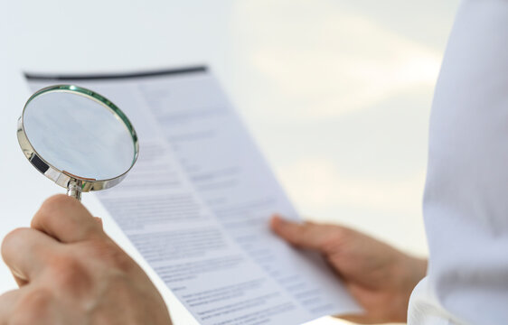 Close-up of hands reviewing document with magnifying glass.  Focus, detail, accuracy concepts.