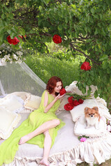 a beautiful girl with dark hair is lying on a bed in the yard. she is holding flowers in her hands