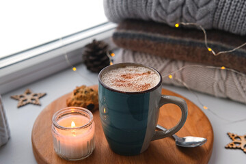 Winter windowsill still life. Blue ceramic cup of hot coffee on window sill. Christmas decorations on the background. Cozy home picture. Warm woolen knitted sweaters, Burn Candle, Cookies. Stock photo