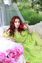 a beautiful girl with dark hair is lying on a bed in the yard. she is holding flowers in her hands