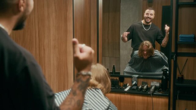 Medium shot of Caucasian barber counting to three after finishing work, surprised client opening eyes, admiring new haircut in mirror, reacting with joy, then thanking hairstylist and bumping fists