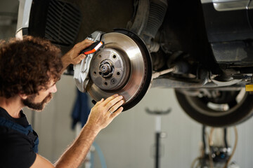 A skilled mechanic inspects and repairs the brake system of a car in a well-lit repair shop. Tools and equipment are organized around him, indicating an active work session.