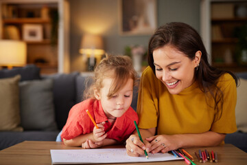 A mother and her young daughter spend quality time together at home, coloring with crayons on a table in their cozy living room. Laughter and creativity fill the air.