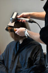 Parrucchiere asciuga i capelli di una cliente con phon professionale e spazzola 