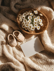 Cozy flat lay with baby shoes, daisies in a basket, and blank card on soft blanket. Ideal for newborn announcement, baby shower, or motherhood themes.
