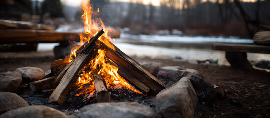 Creative lifestyle template. Campfire bonfire fire burning, wooden chopped tree log trunk stump wood firewood rocks with blurred frozen lake forest outdoor background. copy text space. Long banner