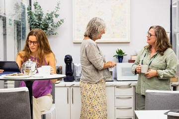 Multigenerational women colleagues relaxing in a modern office kitchen