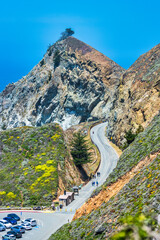 Winding Highway 1 road at Devil Slide Trail near Pacifica California with steep rocky cliffs hillside greenery and a lone tree on top overlooking the Pacific Ocean on a sunny day