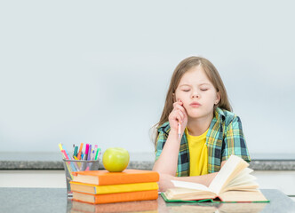 Pensive little girl doing homework at home with books. Empty space for text