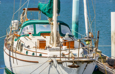 Obraz premium Classic sailboat with green canopy docked at marina. Elegant wooden details and nautical ropes highlight traditional craftsmanship. Peaceful harbor scene on a sunny day, symbolizing travel and