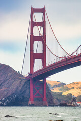 Golden Gate Bridge at sunset seen from Baker Beach, San Francisco. Scenic view with ocean waves, rocks, and dramatic evening sky. Iconic California landmark symbolizing travel, architecture, and