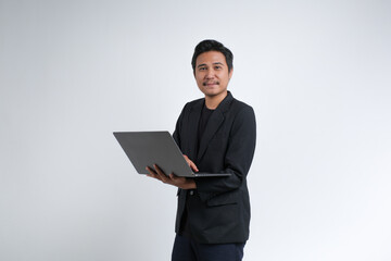 An Asian businessman wearing a blazer holding a laptop with a cheerful expression. Studio shot with...