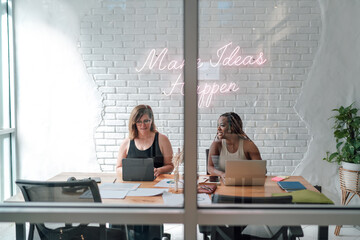 Two female digital professionals work side by side in modern office, using laptop and tablet, symbolizing partnership, technology, and co-creation in freelance economy.