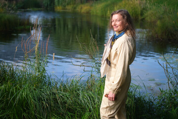 Woman smiling by pond in nature. Happy female enjoying summer travel, peace concept. Healthy lifestyle. Middle-aged woman (50 years old)