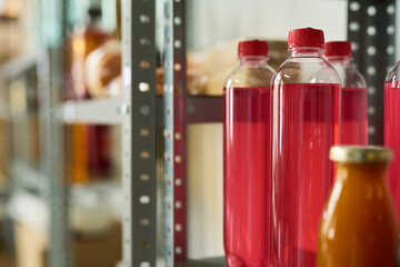 Plastic bottles with red liquid standing on metal shelving in storage room, transparent containers...