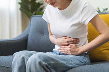 Sick asian young woman in pain, hand holding belly, stomach pain from food poisoning, girl hurt...