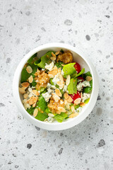 Fresh salad with leafy greens, cherry tomatoes, blue cheese, almonds, and vinaigrette in a bowl on a light speckled countertop. Healthy vegetarian meal, top view