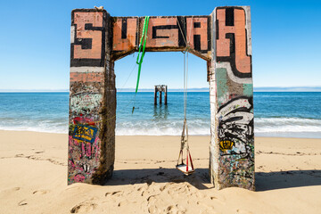 Ruins of the old pier with graffiti and swing at Davenport Pier Beach, California, USA. Iconic coastal landmark near Santa Cruz, where sandy shores meet the Pacific Ocean under blue skies