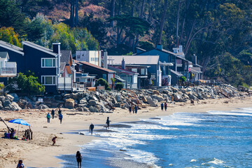 Beachfront houses along the coast of Santa Cruz, California, USA. People walk on sandy beach by the Pacific Ocean, enjoying seaside lifestyle with waves, coastal homes, and scenic shoreline views