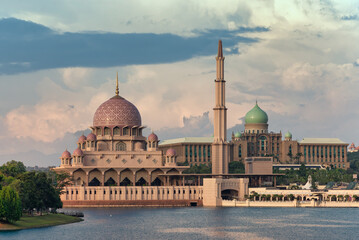 Obraz premium Putra Mosque, pink dome, and Perdana Putra, green domes, across Putrajaya Lake, Putrajaya, Malaysia. Iconic architecture under a cloudy sky in golden hour