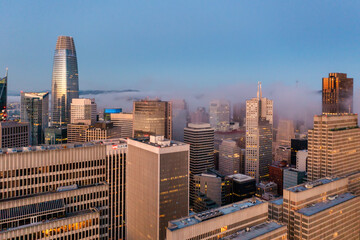 Obraz premium San Francisco downtown skyline at sunset with Salesforce Tower and modern skyscrapers rising above city fog. Iconic urban view of California, USA, showcasing architecture, business, and evening lights