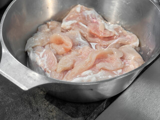Raw chicken breast in metal bowl for cooking preparation.