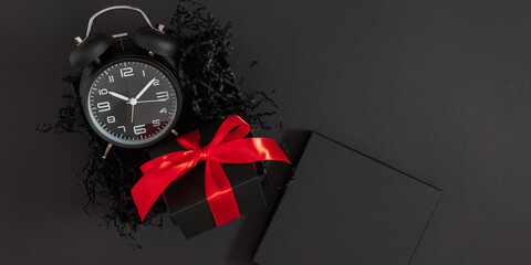 Open black box with black alarm clock and red satin ribbon on dark background. Black Friday Sale!
