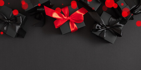 Festive, wide composition of black gift boxes with black and red ribbons on a black background with shadow and bokeh creates a Black Friday sales theme.