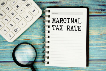 Marginal Tax Rate text on notepad with magnifying glass and calculator on wooden background