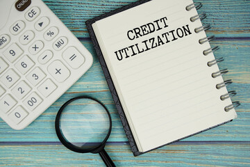 Credit Utilization text on notepad with magnifying glass and calculator on wooden background