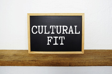 Fototapeta premium Cultural Fit text written on blackboard with wooden shelf and concrete background