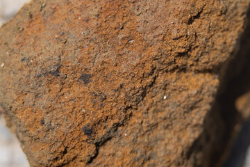 Texture of a rough rock showing orange and brown mineral details under natural light in an outdoor setting