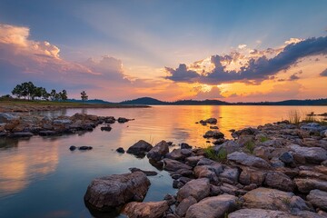Scenic Sunset Over Rocky Riverbank with Calm Water and Cloudy Sky