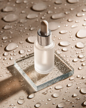 Boccetta contagocce in vetro satinato con gocce d&rsquo;acqua su piastra di vetro. Atmosfera fresh e igienica, ideale per visual di siero viso e cosmetici idratanti.