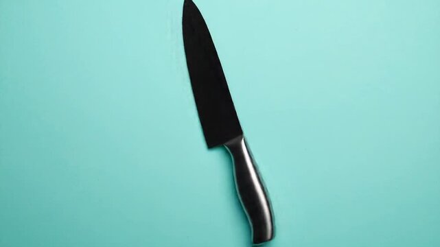 Studio Shot of Black Kitchen Knife with Serrated Edge and Metallic Handle on Teal Background Food Preparation Tool Equipment Butcher Implement Cutlery