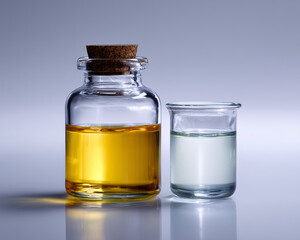 Bottiglia in vetro con olio cosmetico giallo accanto a becher con soluzione acquosa. Still life pulito per cosmetica naturale e formulazioni skincare.
