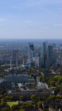 Vertical 4K drone video sweeps London SE1: Strata Vauxhall tower, rising cranes and leafy estates under a clear blue sky - perfect stock for urban growth, architecture and travel features.
