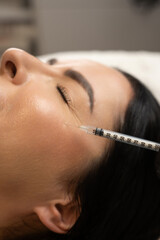 Close-up of a woman receiving a cosmetic injection near the eye area. A syringe is applied to the...