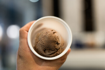 Chocolate ice cream scoops in plastic cup on hand