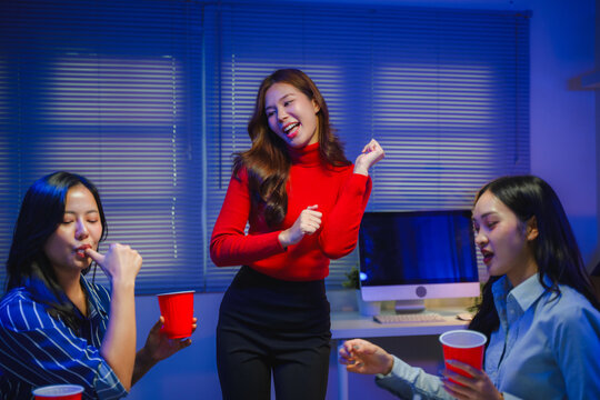 Diverse Asian businesswomen enjoying office party after working hours, dancing and having fun with red cups